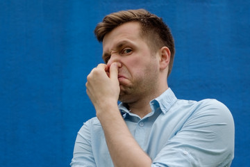 portrait of young caucasian man closing his nose because of terrible smelling