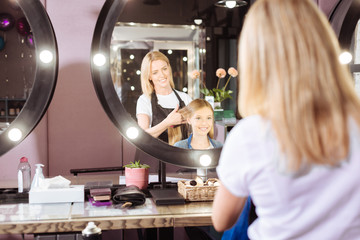 Charming hairdresser brushing hair of her client