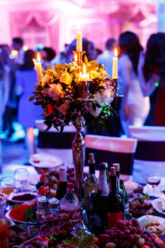 Candles shine in rose bouquet on dinner table