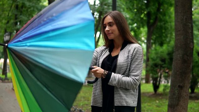 Beautiful woman checking if it is raining or not then opening her colorful umbrella standing in the city park. Slowmotion shot