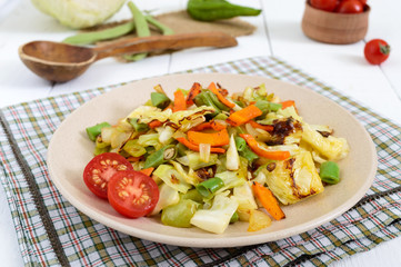Vegetable stew - a mixture of baked cabbage, green beans, onions, carrots, cherry tomatoes, sweet pepper on a plate on a white wooden background. Vegan cuisine. Proper nutrition.
