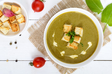 Light vegan spinach cream soup with crispy croutons in a bowl on a white background.