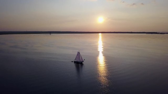 Aerial: flying backwards from a sailing ship at sunset with beautiful backlight
