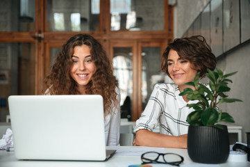 Two pretty smiling women working by the laptop