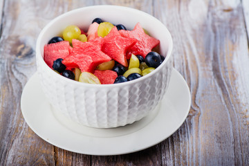 Fresh summer watermelon salad with blueberry and grapes on wooden table. Copy space