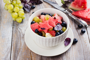 Fresh summer watermelon salad with blueberry and grapes on wooden table. Copy space