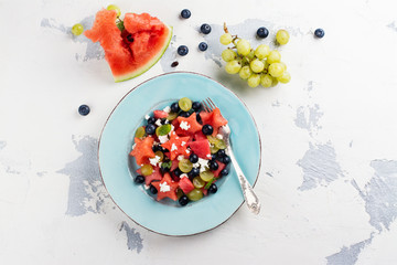 Fresh watermelon salad with feta cheese and berries on white stone table. Top view. Space for text