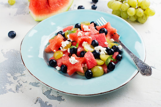 Fresh watermelon salad with feta cheese and berries on white stone table. Space for text