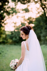 Bride with dark curly hair looks over her shoulder while she stands on the lawn