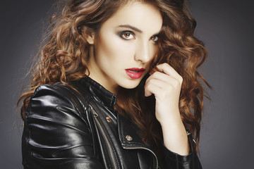 Fototapeta na wymiar Beautiful young woman posing in black leather jacket over grey background. Fashion concept.