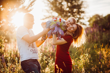 Mom and dad hold their son up standing on the field full of sunlight