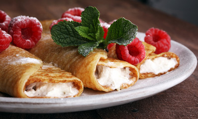 Homemade crepes served with fresh raspberrries and powdered sugar on rustic wooden table