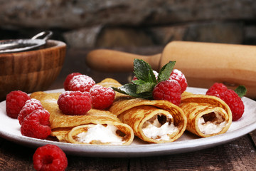 Homemade crepes served with fresh raspberrries and powdered sugar on rustic wooden table