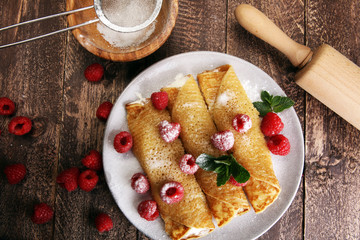 Homemade crepes served with fresh raspberrries and powdered sugar on rustic wooden table