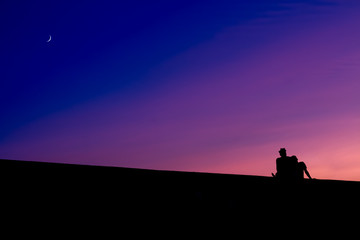 The silhouettes of two men sitting, at sunset.