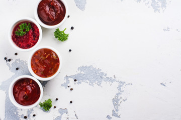 Bowls of various tomato sauces on white stone table. Top view. Copy space