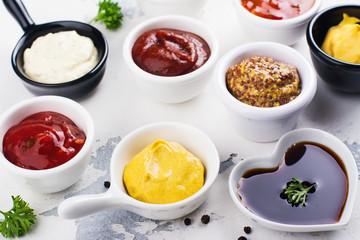 Various sauces and dips in porclean bowls on white stone background. Copy space