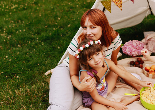 Mother hugs her little firl in flower wreath sitting on plaid outside