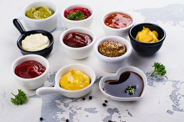 Various sauces and dips in porclean bowls on white stone background. Copy space