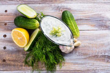 Greek tzatziki sauce with ingredients on kitchen wooden table. Copy space