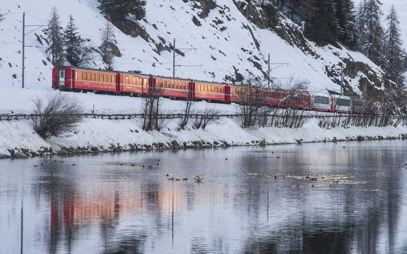 Bernina Red Train reflected in the river at Celerina in Engadin - Switzerland during winter