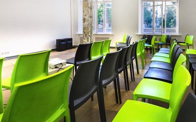 Empty lecture hall - small class room with green and black plastic chairs and big bright windows. Comfort space for learning.
