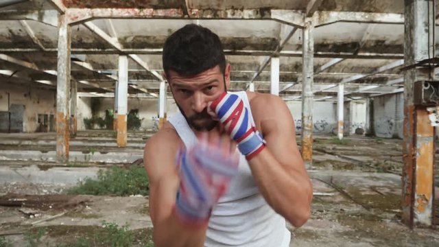 Angry male boxer doing shadow boxing exercise in an old abandoned building looking at camera.
