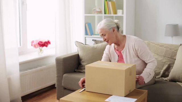 happy senior woman opening parcel box at home
