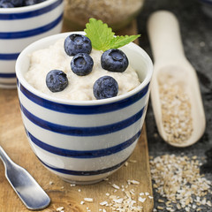 Healthy breakfast: milk porridge from oat bran on skimmed milk with honey, juicy blueberries, pecans on a simple wooden background with a spoon and a jar of honey. Top View.