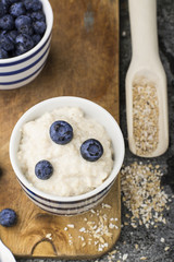 Healthy breakfast: milk porridge from oat bran on skimmed milk with honey, juicy blueberries, pecans on a simple wooden background with a spoon and a jar of honey. Top View.
