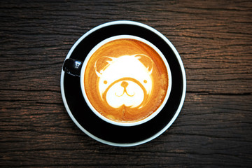 Bear face latte art coffee in black cup on old wooden desk , top view and copy space