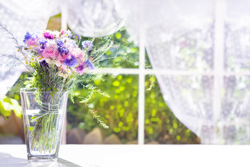 Bouquet of field flowers  in glass vase near the window