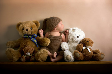 Newborn baby boy wearing a brown knitted bear hat and pants, sleeping on a shelf