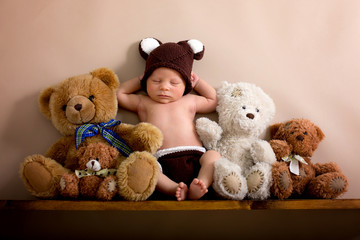 Newborn baby boy wearing a brown knitted bear hat and pants, sleeping on a shelf