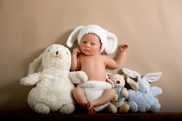 Newborn baby boy wearing a brown knitted rabbit hat and pants, sleeping on a shelf