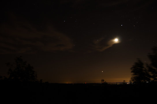 Distant village lights visible under the moon, stars and clouds of o warm summer night near Heflin, Alabama, USA.