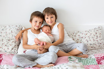 Fototapeta na wymiar Two children, toddler and his big brother, hugging and kissing their newborn baby brother at home