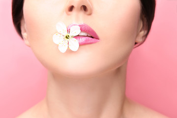 Fototapeta na wymiar Beautiful young woman with flower between lips on color background