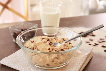 Raw dough with chocolate chips and spoon in bowl on kitchen table