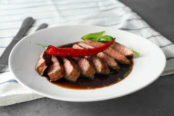 Plate with delicious sliced meat and sauce on table