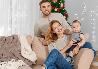 Happy parents with baby in decorated room for Christmas