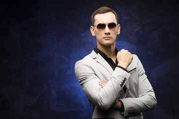 man in a gray suit and sunglasses on a blue background.