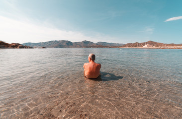 Aged man looking the horizon at the beach inside the water - Sardinia
