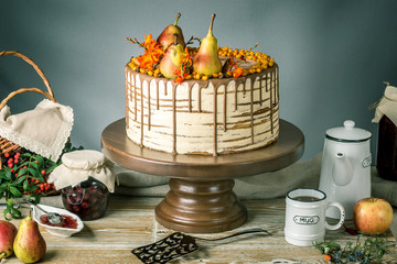 Honey cake pour over the chocolate and decorated with pears and sea buckthorn on a wooden table. Sweet autumn still life