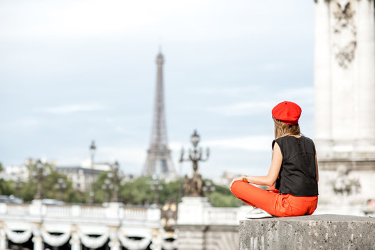 Young woman in red hat enjoying great view on Eiffel tower sitting on the bridge in Paris