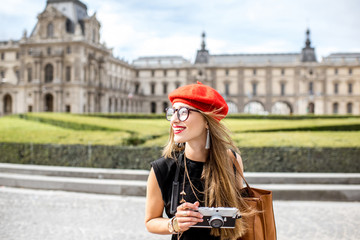 Young woman tourist in red cap walking with photo camera near the famous Louvre museum in Paris
