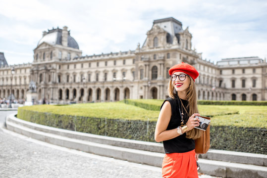 Fototapeta Young woman tourist in red cap walking with photo camera near the famous Louvre museum in Paris