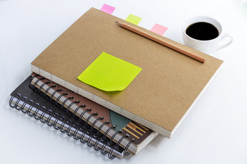 coffee cup with notebook and blank yellow paper note on white table.