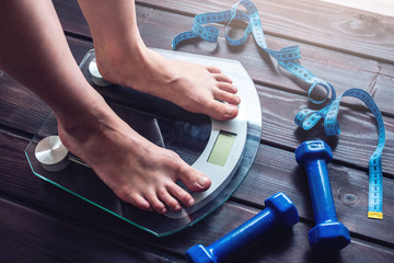 Female feet standing on electronic scales, dumbbells and measuring tape. Concept of slimming and weight loss