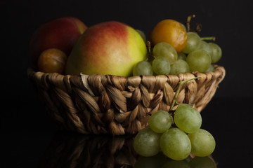 Assorted fruits. Apple, plum and grapes in a basket on a black background